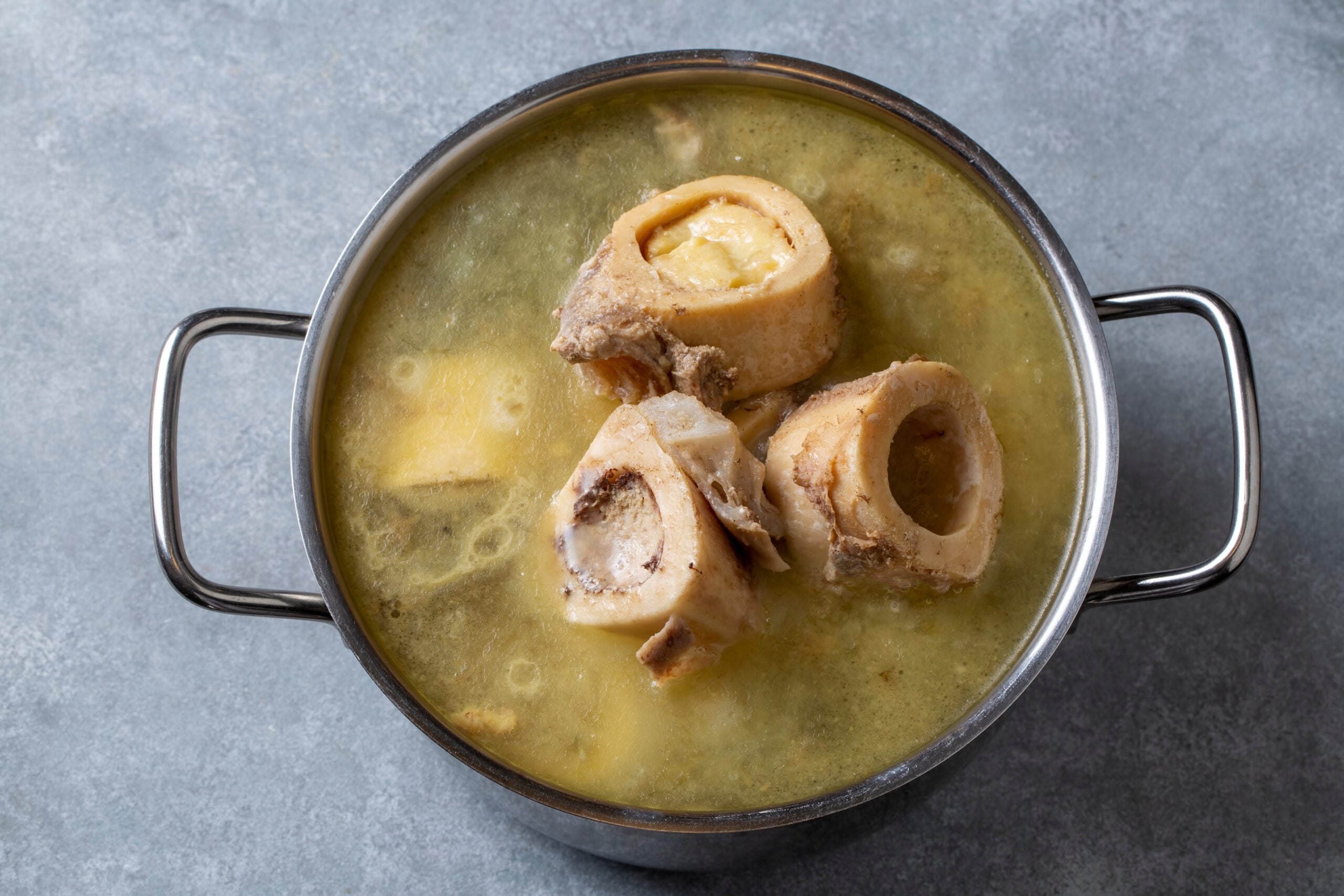 A pot of bone broth simmering with bones and broth on the stove