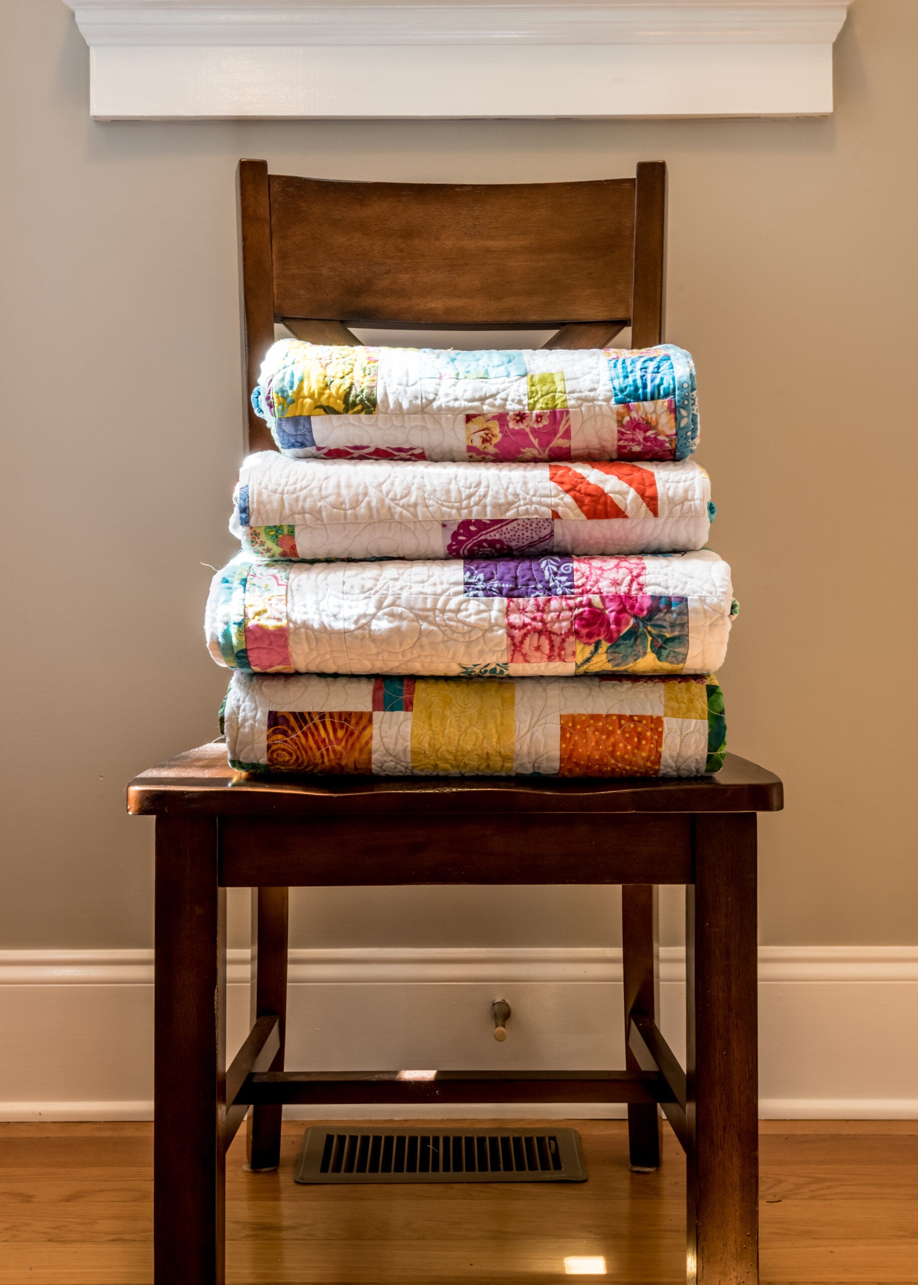 A stack of folded wool blankets and a worn quilt draped over a wooden chair