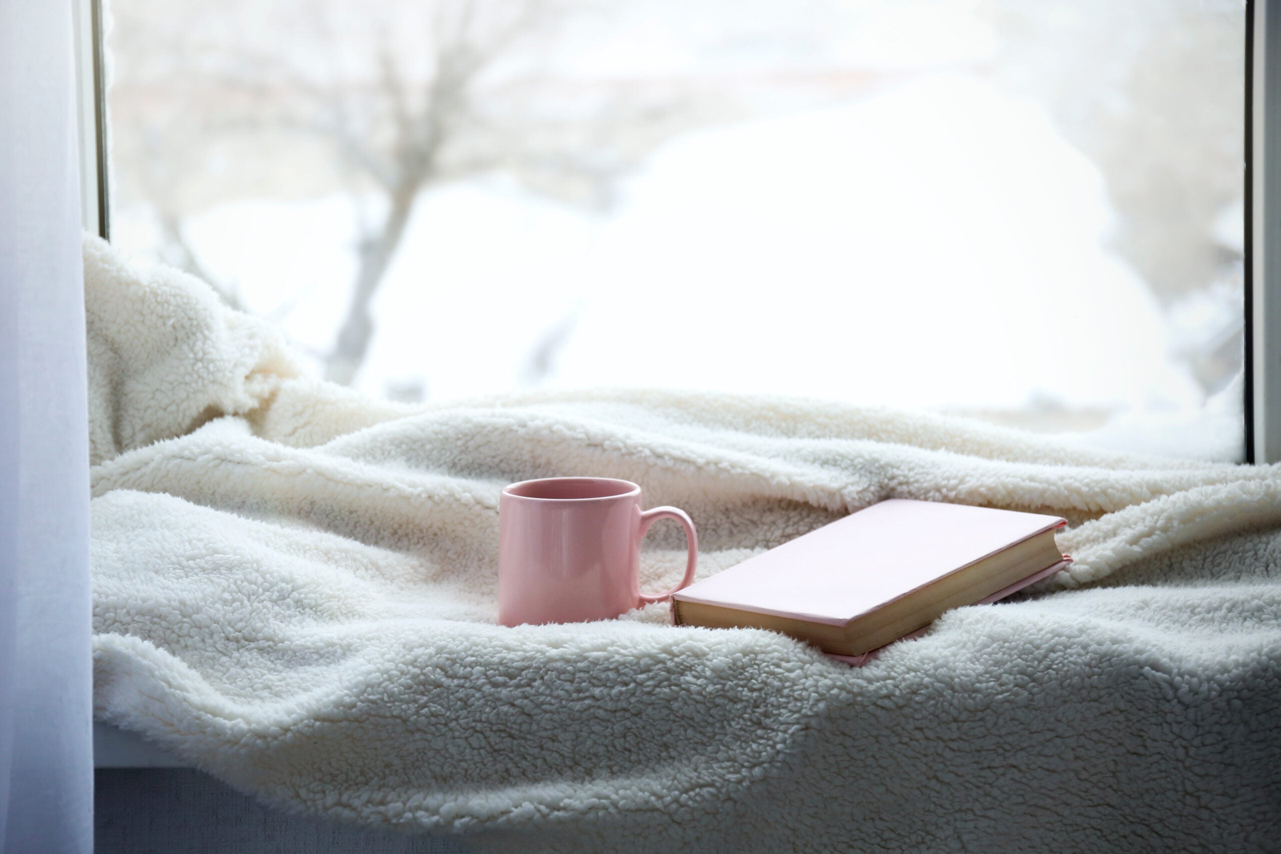 A cup of tea and a warm blanket in a reading nook by the window