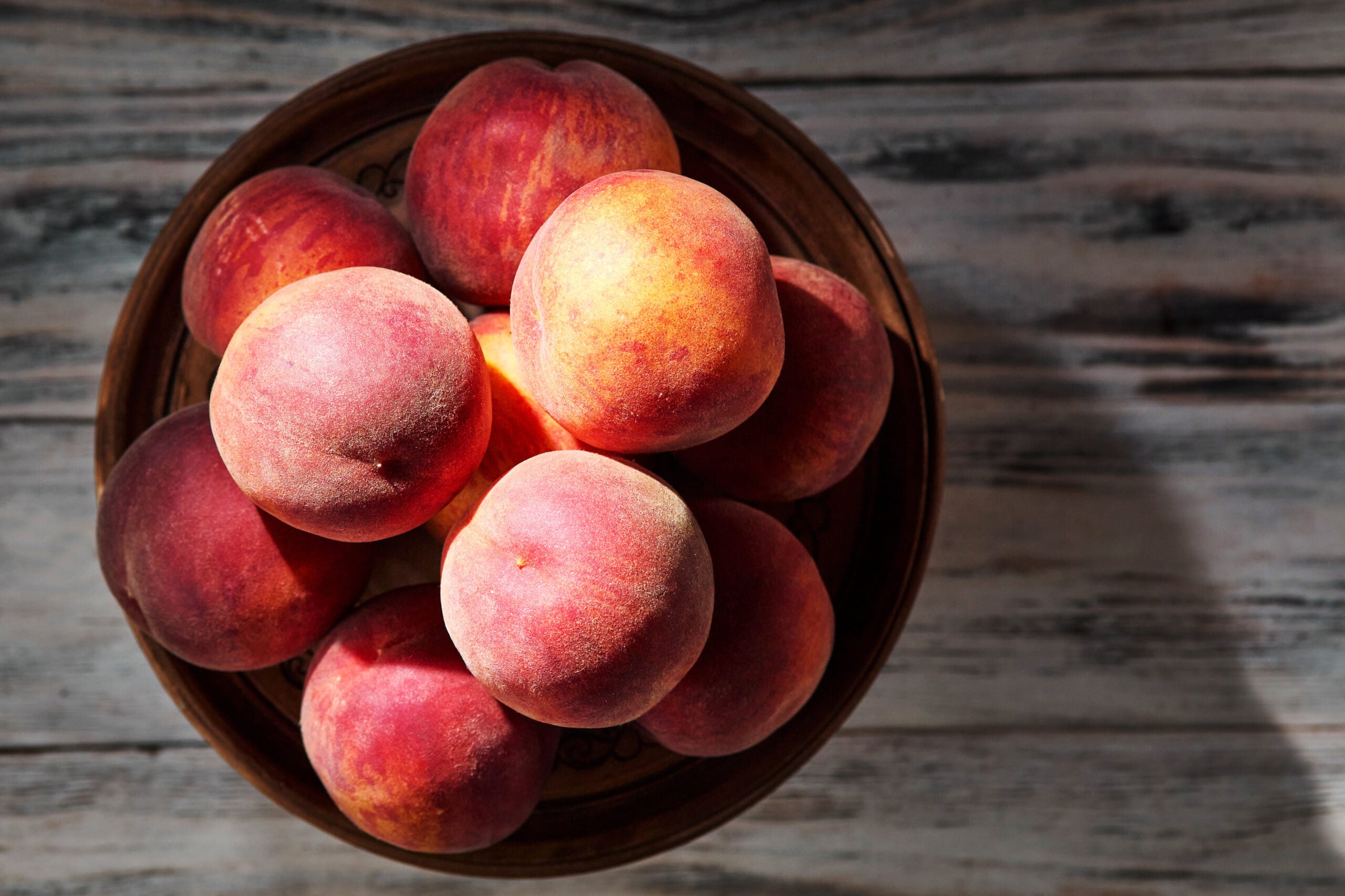 Fresh ripe yellow peaches on a clay plate on a rustic wooden table