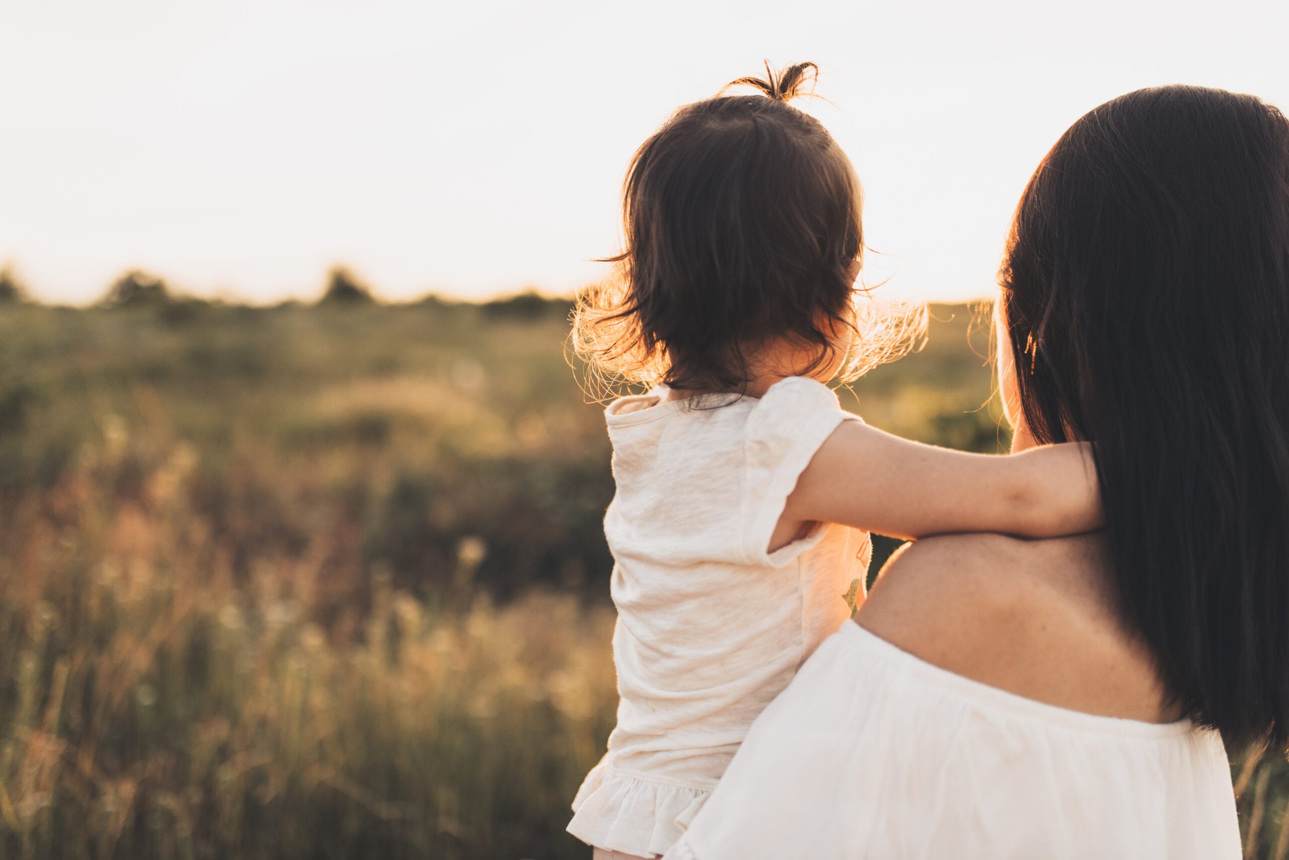 A mother and young child seen from behind together outdoors