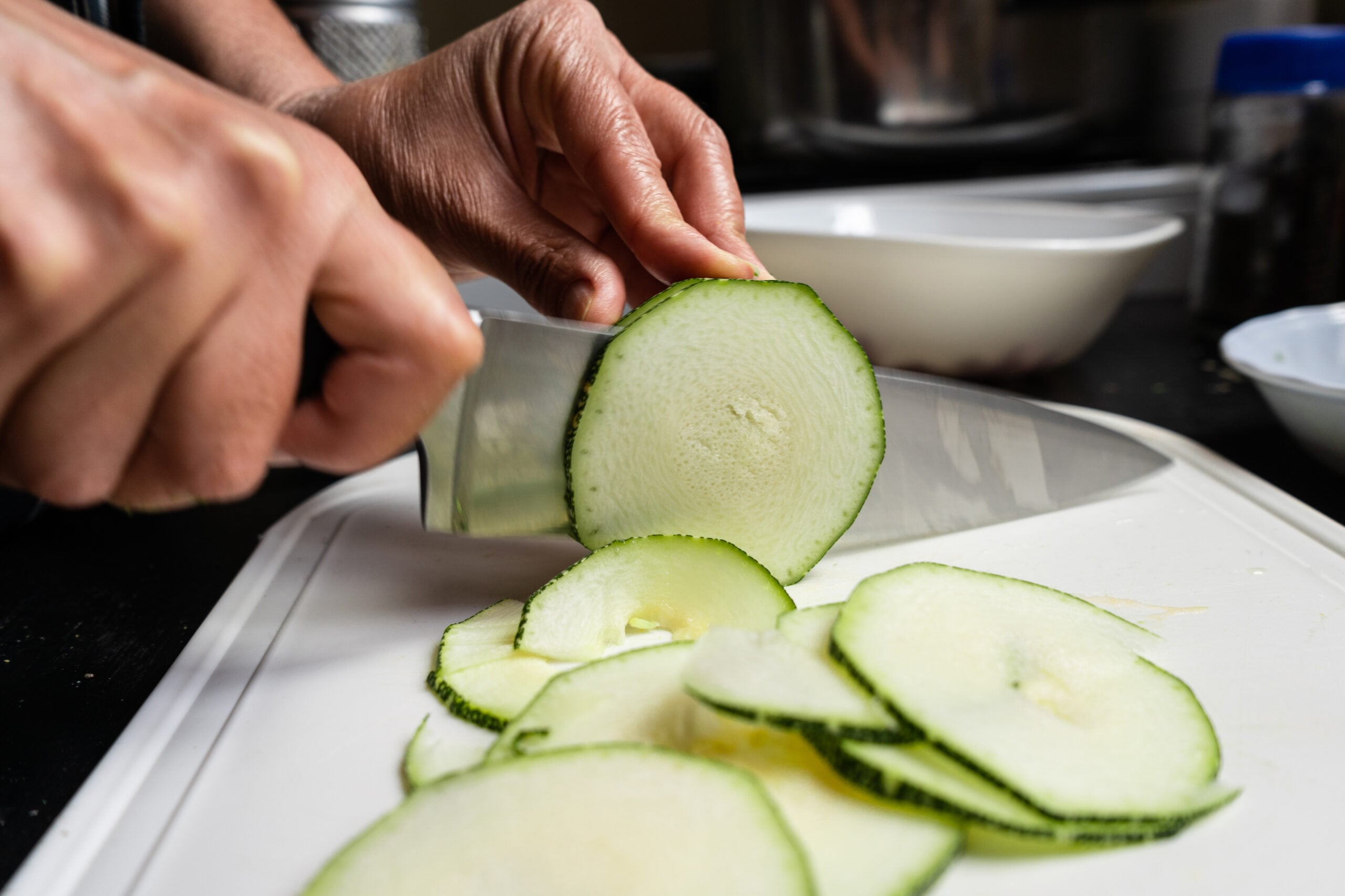 Fresh zucchini being sliced on a cutting board before shredding for zucchini bread