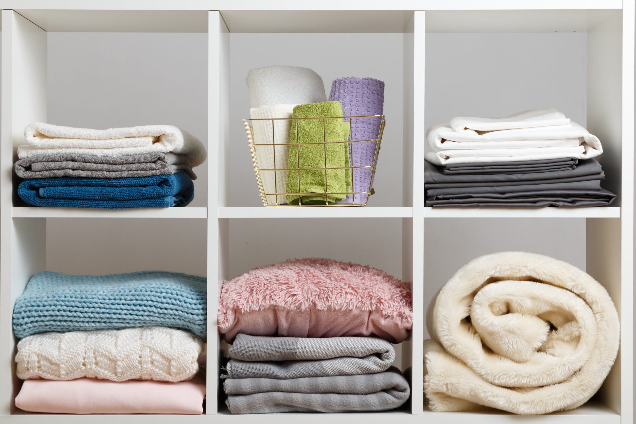 Neat stacks of folded linens, blankets, and clothes on a simple white shelf