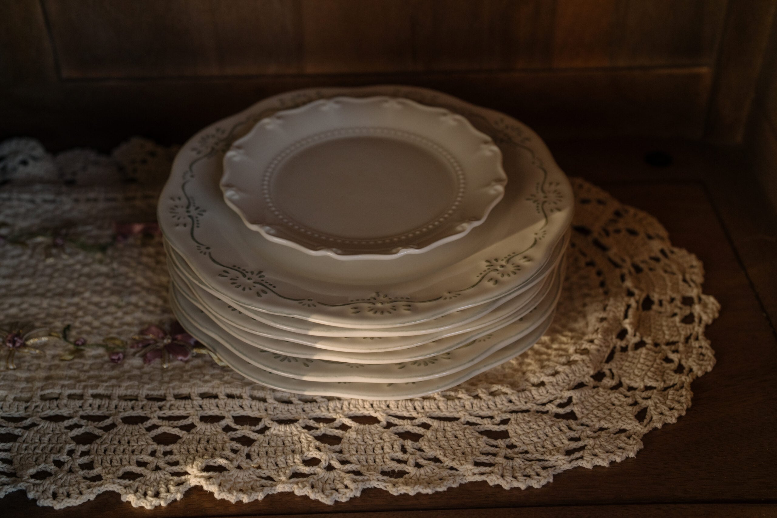 A simple stack of vintage plates on a wooden kitchen shelf in soft warm sunlight