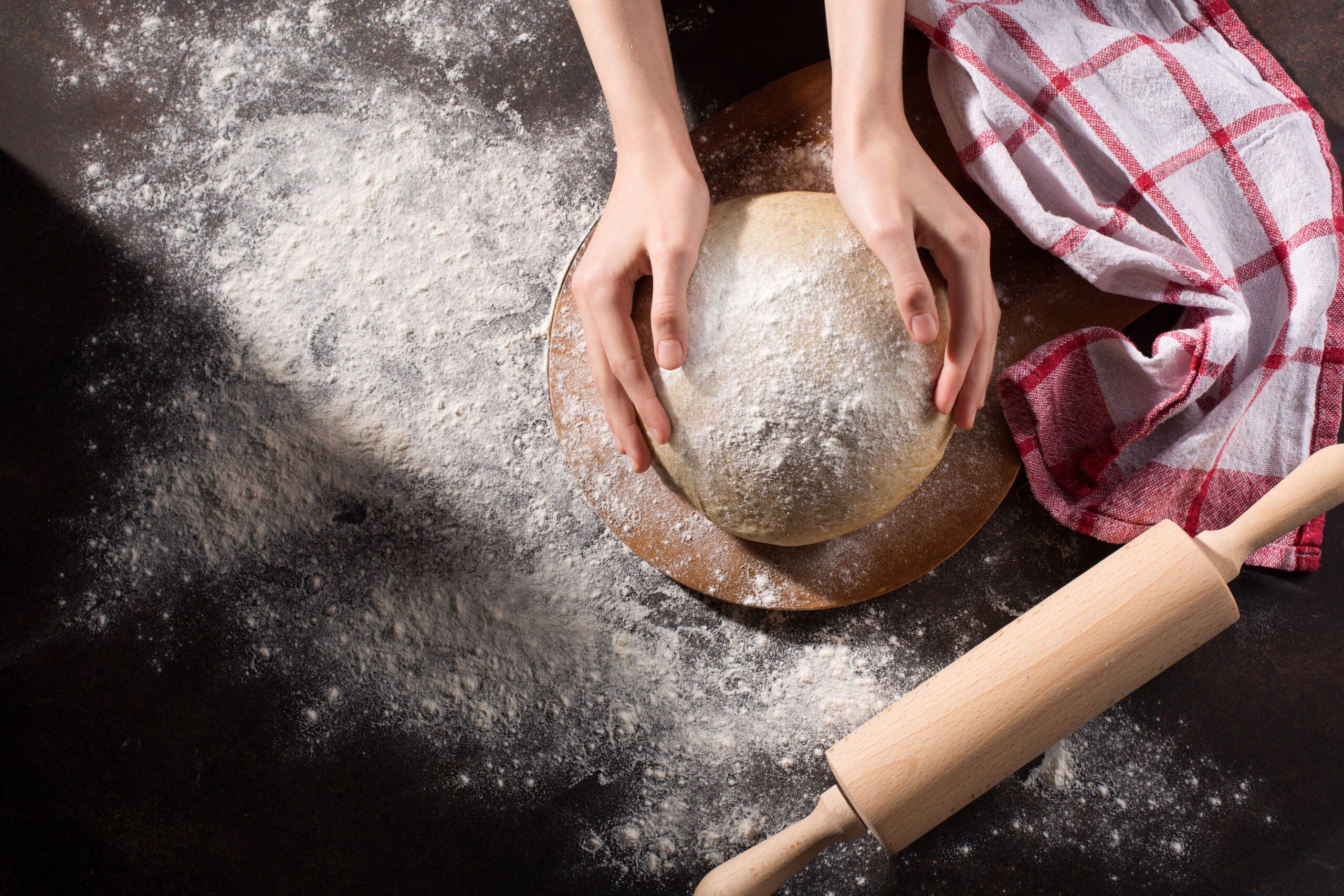 Hands working all butter pie crust dough on a floured wooden table with a rolling pin