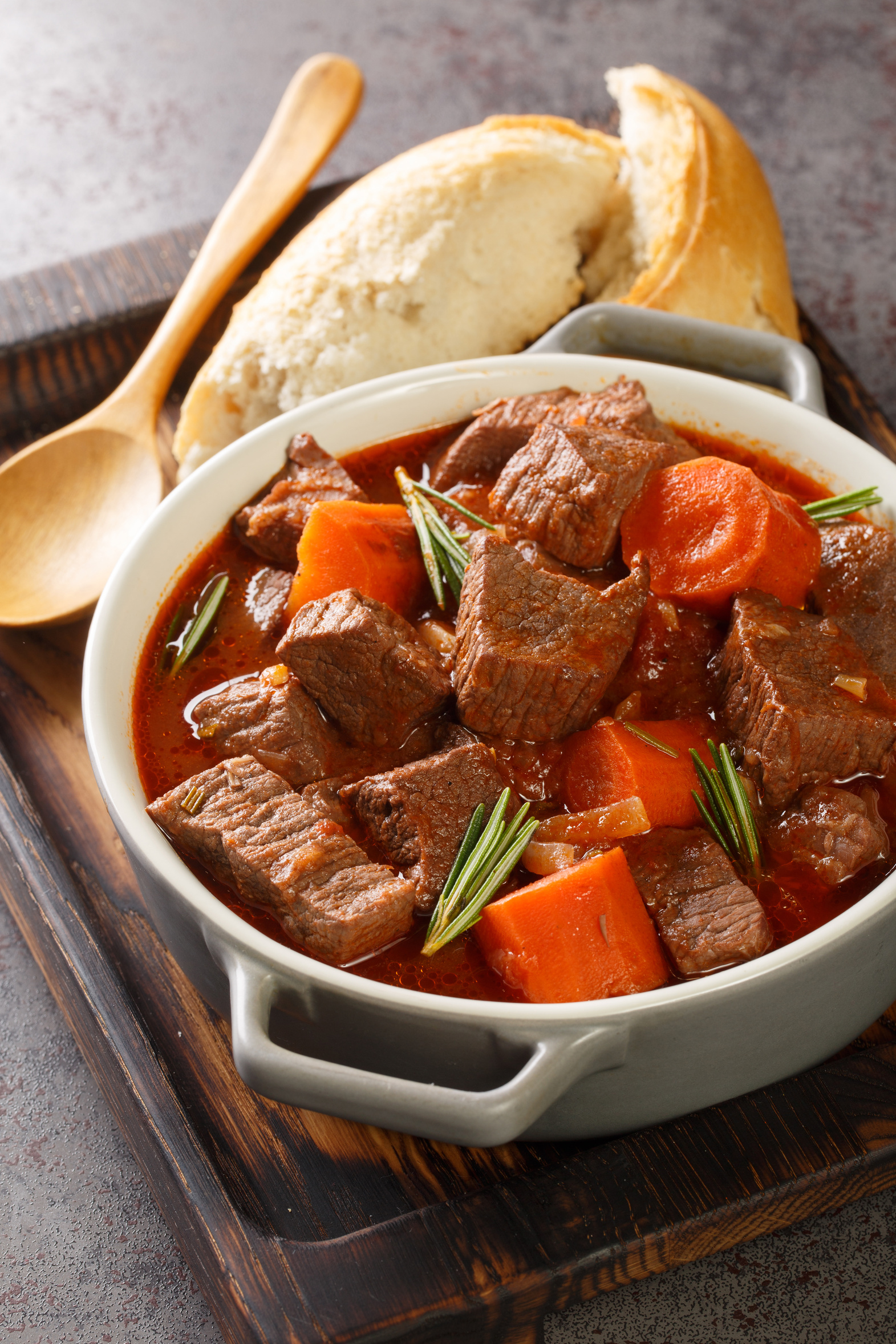 Bowl of braised beef stew with vegetables on a wooden tray on a farmhouse table