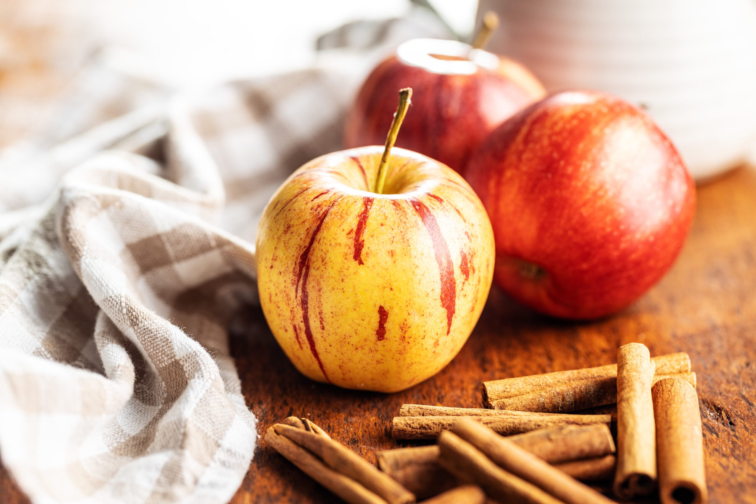 Fresh red autumn apples and cinnamon sticks on a wooden surface, the ingredients for crockpot apple butter