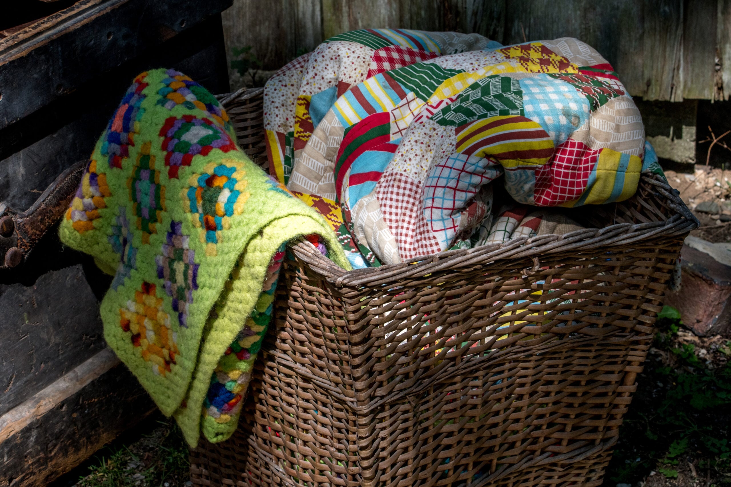 Old wicker basket filled with folded handmade quilts and wool blankets in a farmhouse living room
