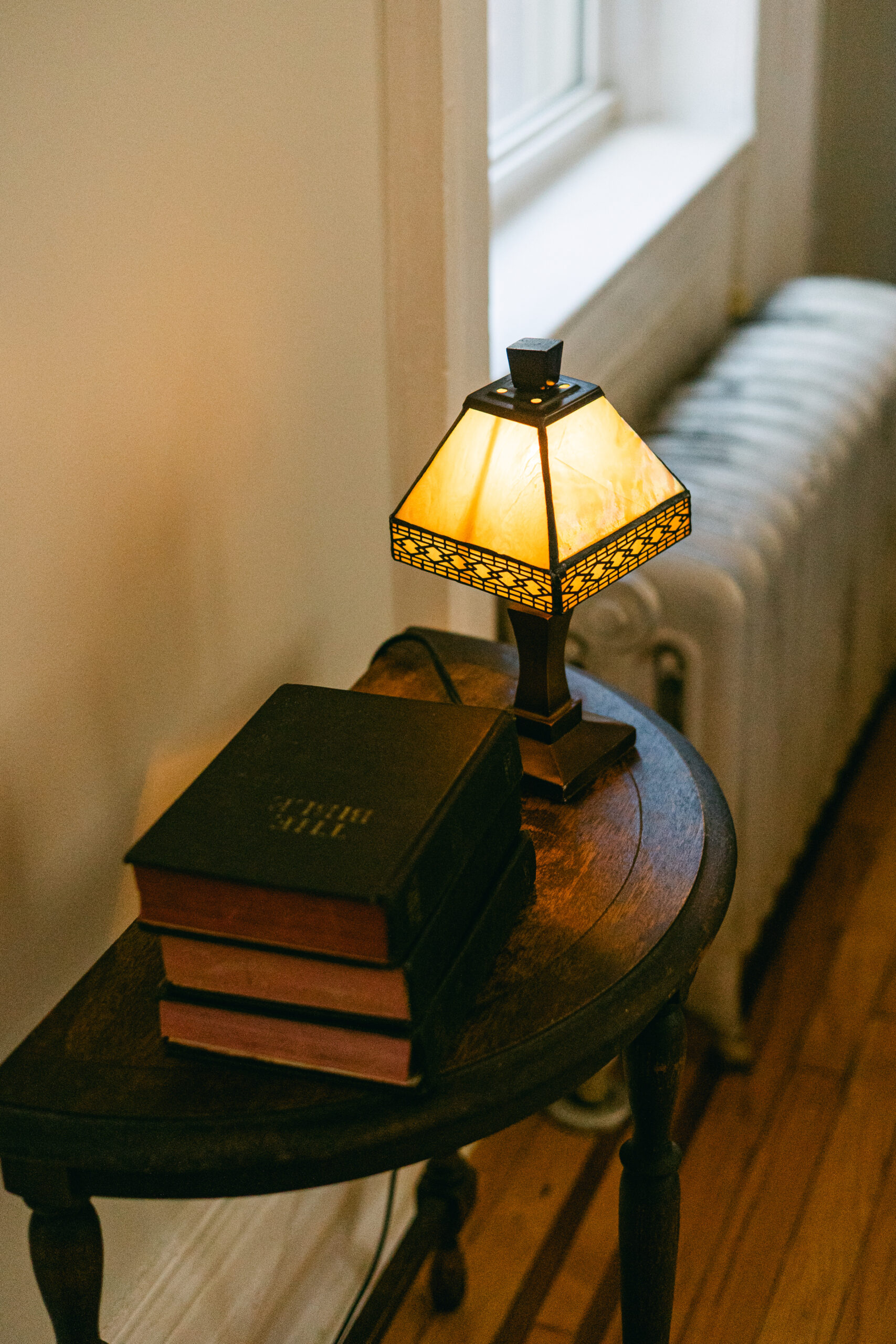 Warm table lamp glowing in a cozy farmhouse reading nook with books beside a window