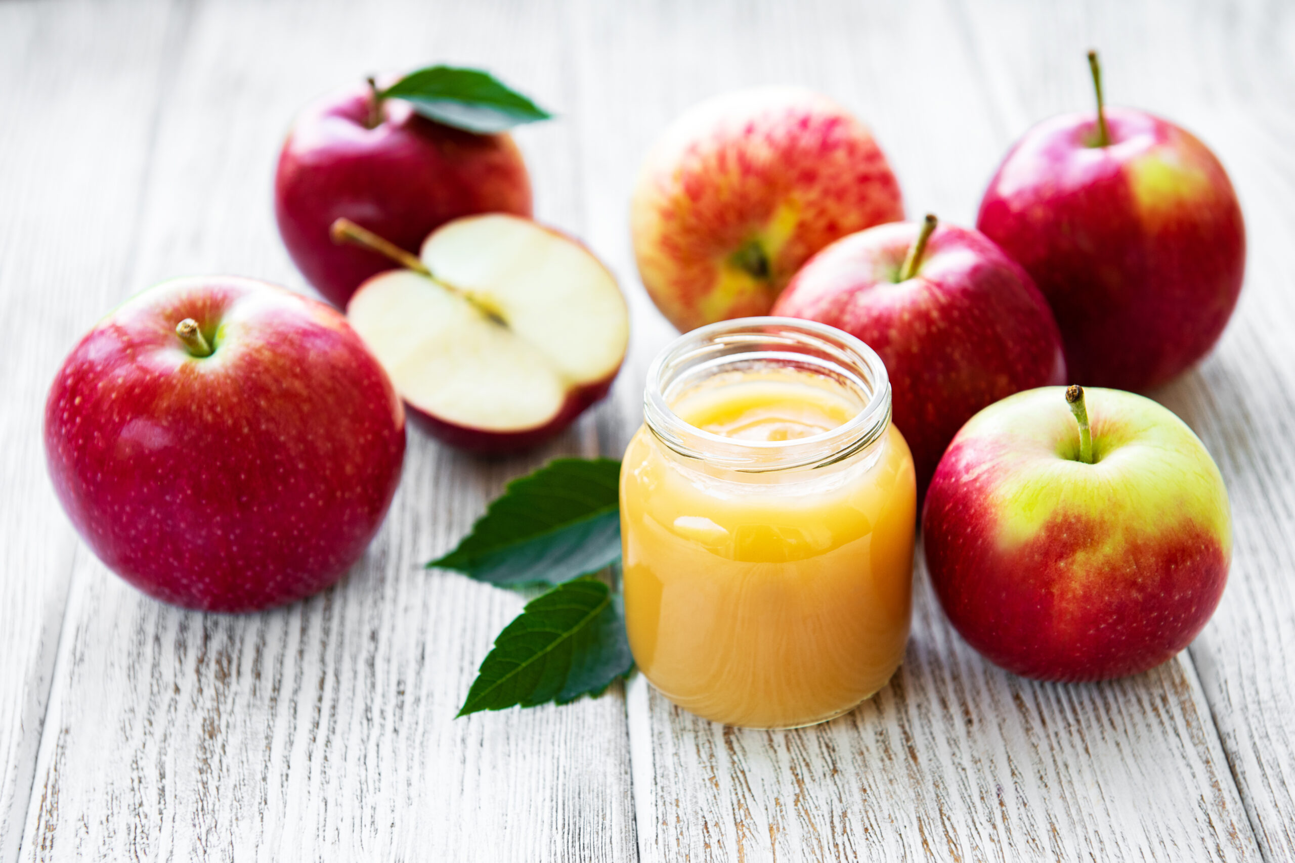 Homemade applesauce in a glass jar with fresh apples beside it on a kitchen counter