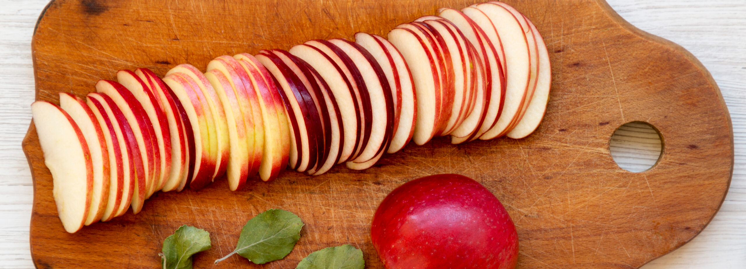 Sliced red apples on a wooden cutting board, cut thick for freezer apple pie filling