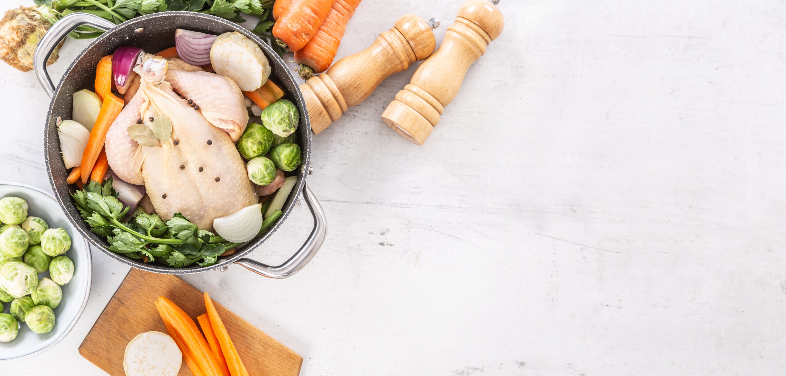 Whole chicken with carrots, celery, onion and herbs laid out to start homemade chicken noodle soup broth