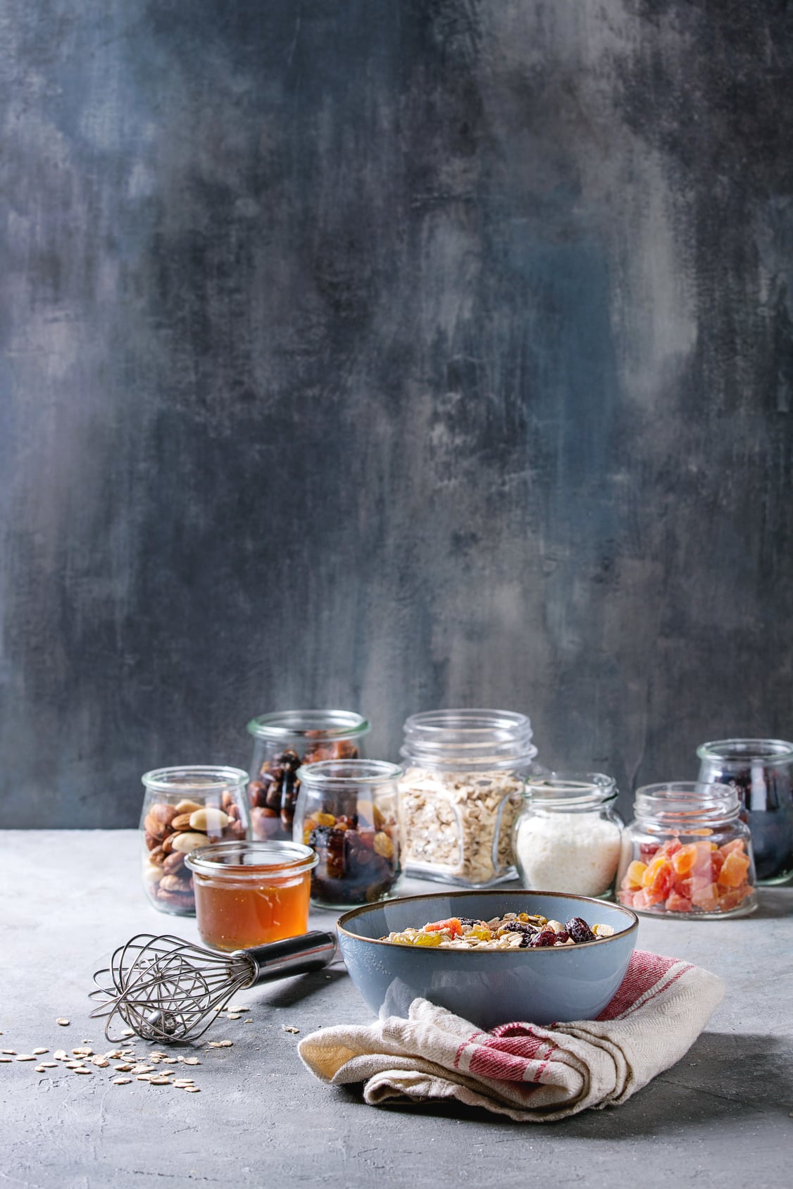 Rolled oats, nuts, dried fruit and honey in bowls and glass jars, the ingredients for an easy homemade granola recipe