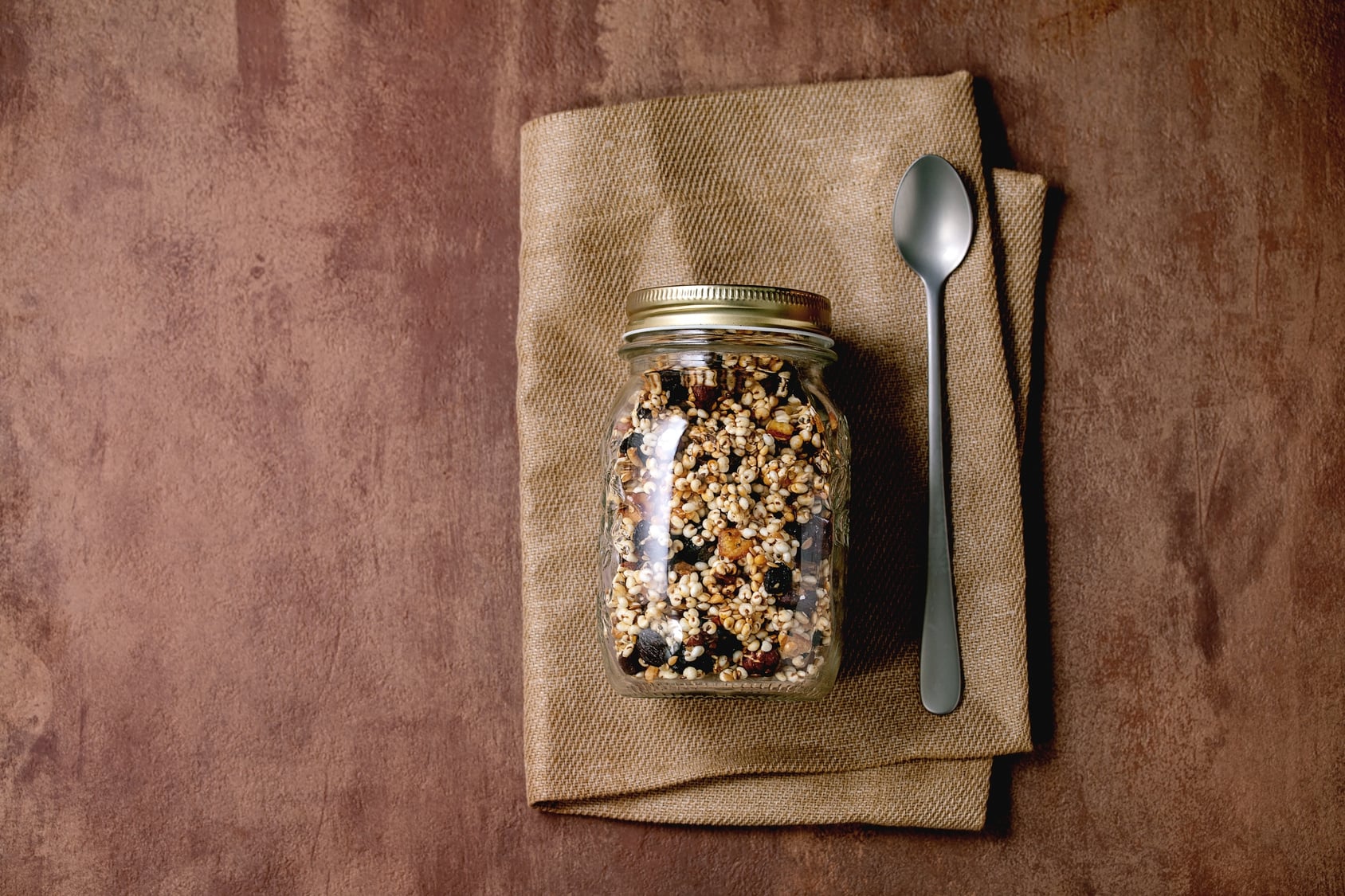 Homemade granola with dried fruit and nuts stored in a glass jar with a spoon on a linen napkin