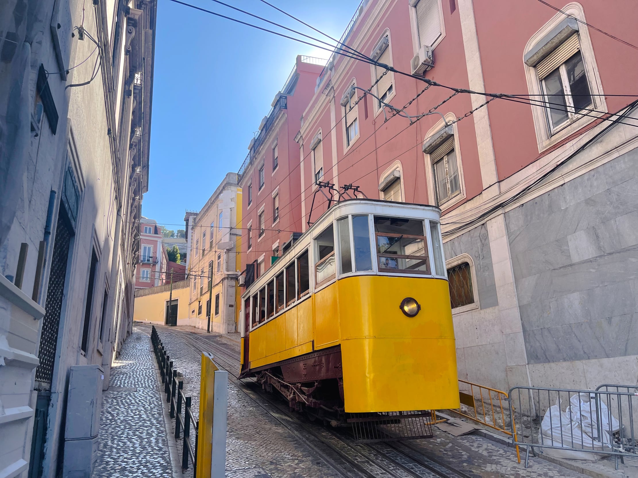 Yellow funicular tram climbing a steep cobbled street between colorful buildings in Lisbon, Portugal