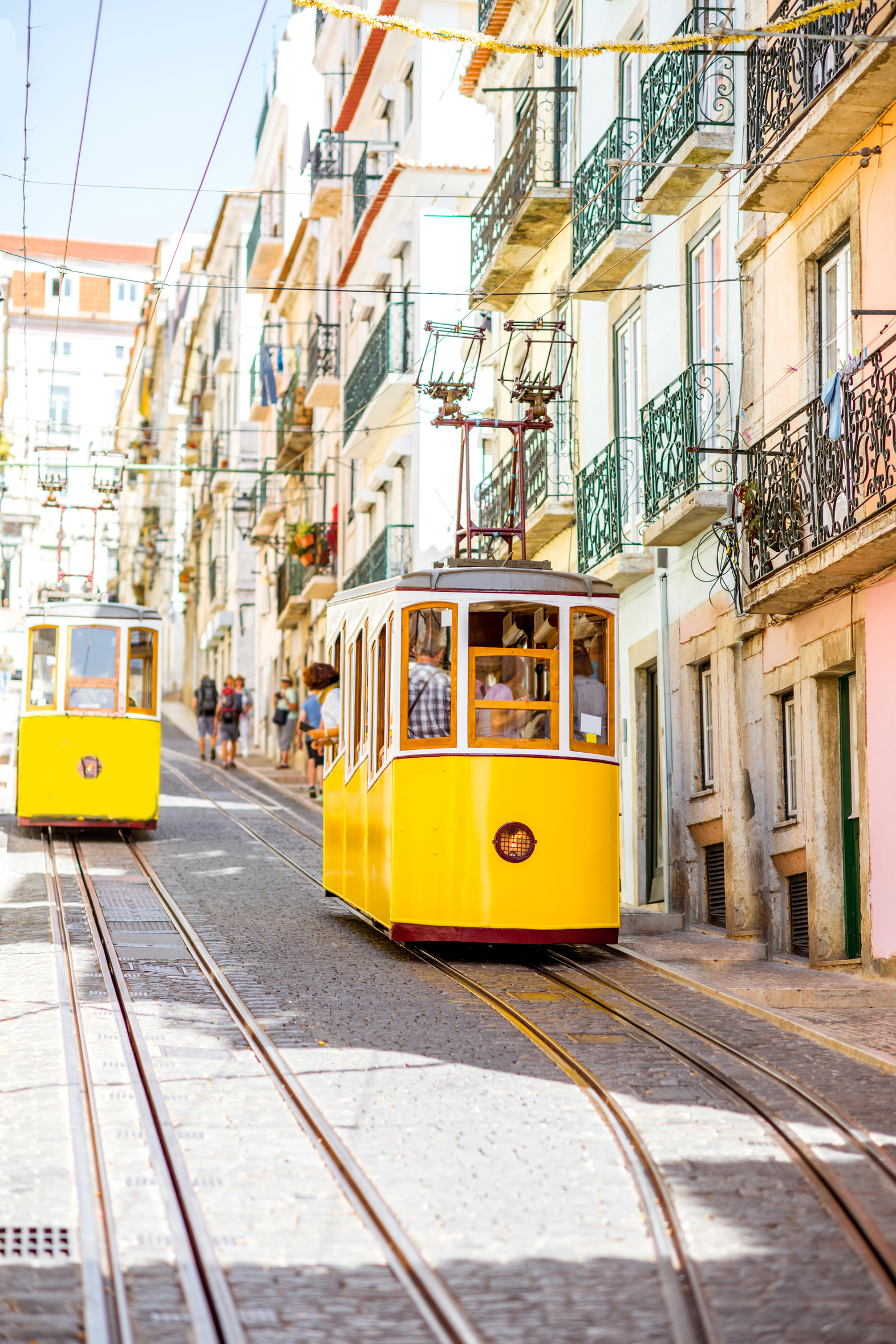 A yellow funicular tram climbing a steep cobblestone street in Lisbon, Portugal