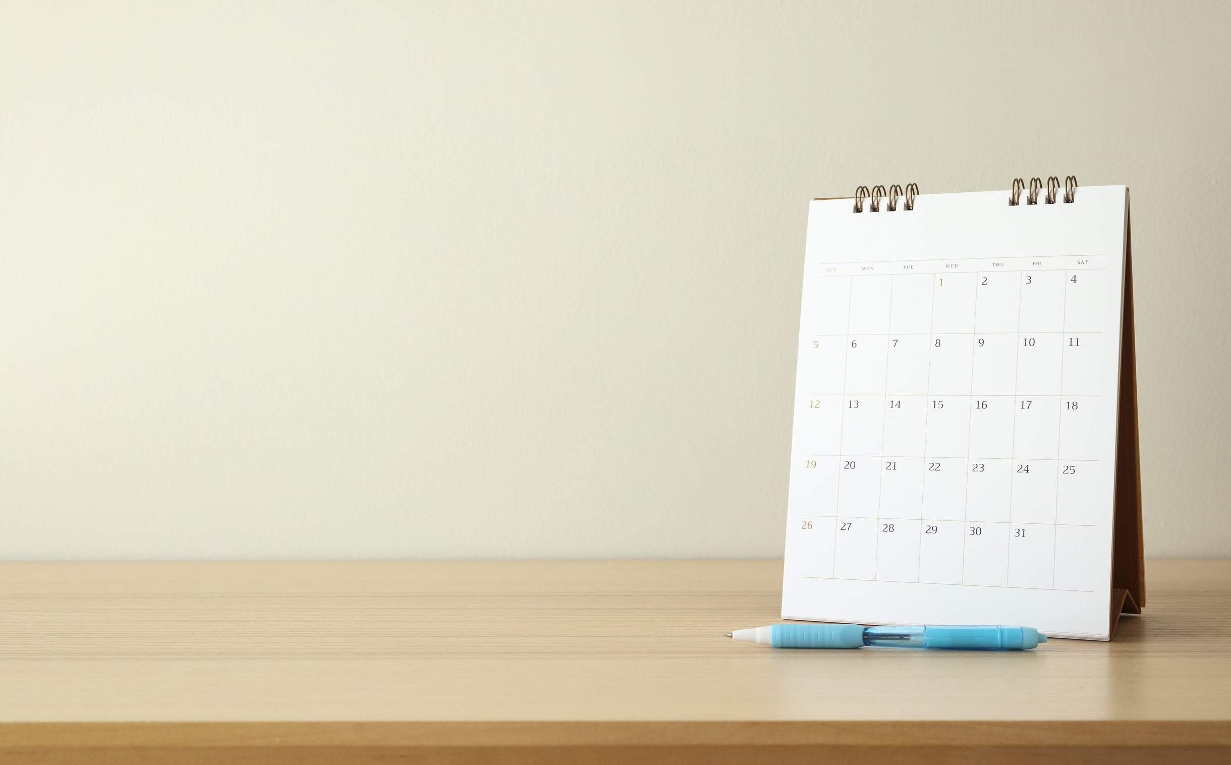 A paper calendar page open on a wooden table next to a pen and a notebook