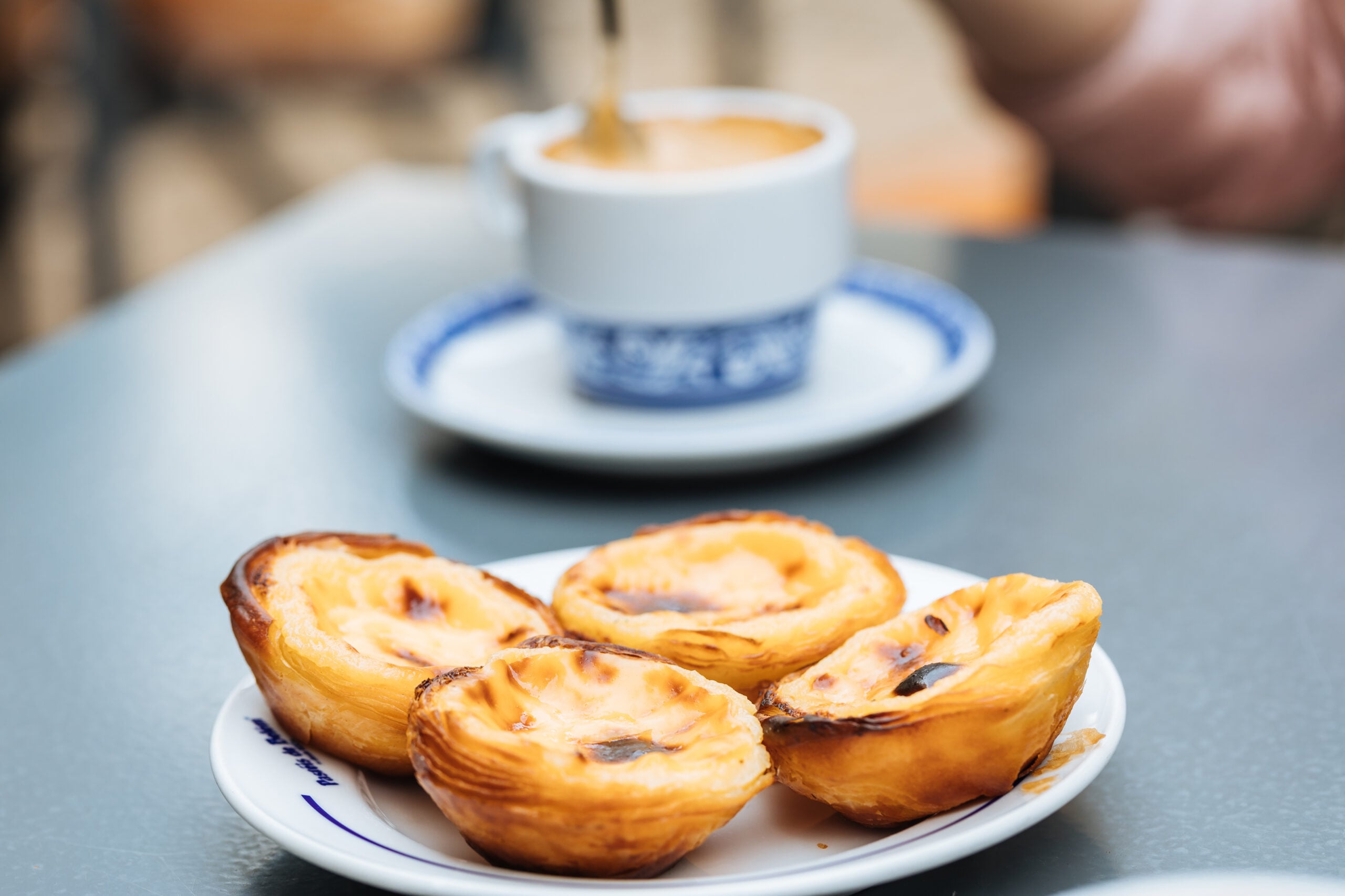 Two pasteis de nata custard tarts beside two coffees on a cafe table in Portugal
