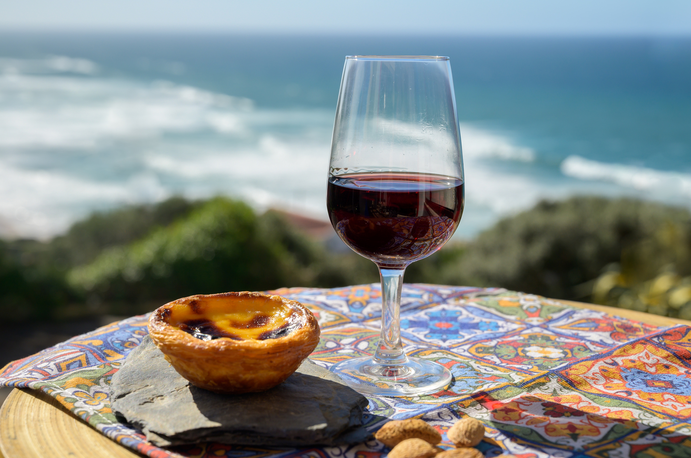 A pastel de nata custard tart on a table with the blue Atlantic behind it on the coast near Lisbon, Portugal