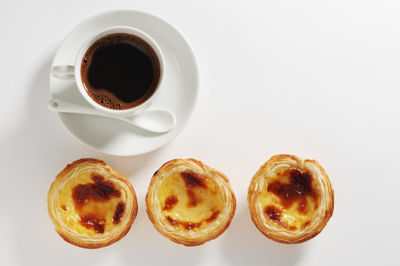 Portuguese pastel de nata custard tart beside a cup of coffee on a cafe table in Portugal