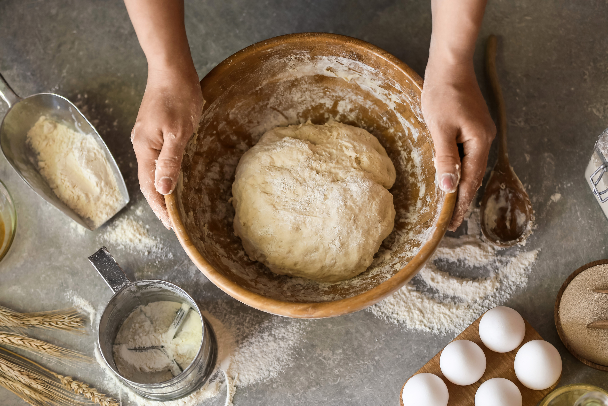Hands shaping soft dinner roll dough on a floured kitchen table